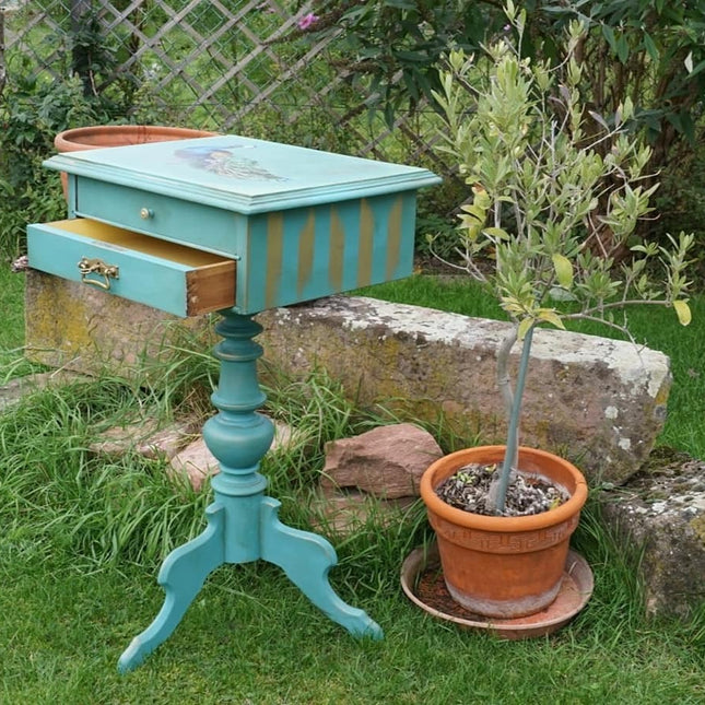 Nähschränkchen gestrichen in Türkis mit einem Pfau auf dem Deckel und goldenen Streifen an der Seite.