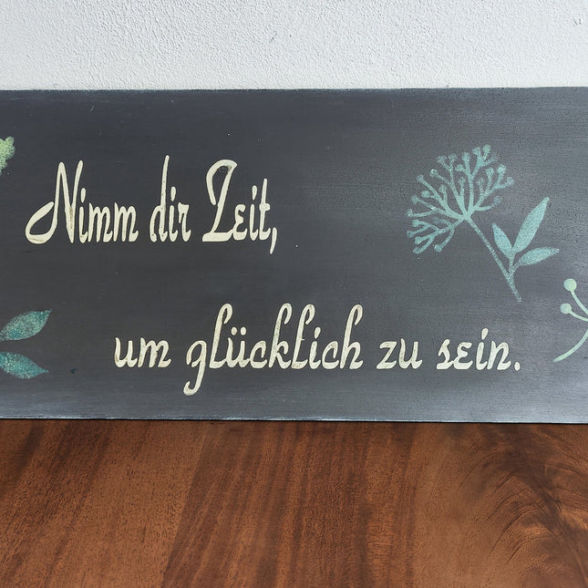 Ein Schild aus unserem Workshop in schwarz mit Blättern und dem Spruch Nimm Dir Zeit um glücklich zu sein.