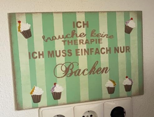 Ein Schild mit grün weißen Streifen mit der Aufschrift: Ich brauche keine Therapie ich muss einfach nur Backen.