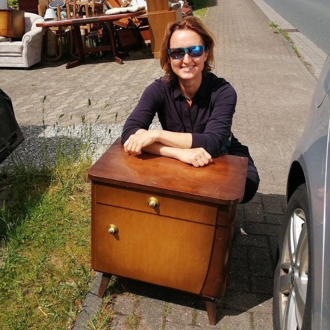 Frau mit Sonnenbrille hinter einem  unbehandelten Nachtkasten (Straßenfund).