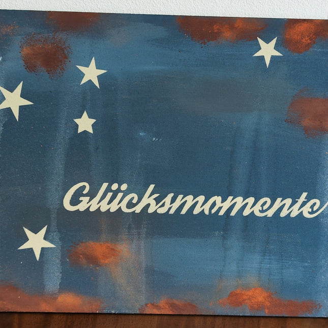Ein blaues Schild mit Rosteffekt mit Sternen und der Aufschrift Glücksmomente aus dem Schilderworkshop.