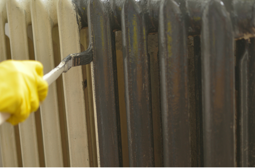 Das Bild zeigt eine Heizung die mit einem Pinsel gestrichen wird.